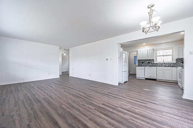 unfurnished living room with a chandelier, baseboards, dark wood-style floors, and a sink