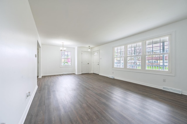 unfurnished living room with dark wood-type flooring, visible vents, baseboards, and an inviting chandelier