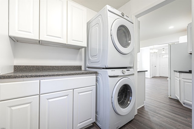 clothes washing area featuring stacked washer / drying machine, recessed lighting, dark wood finished floors, and cabinet space