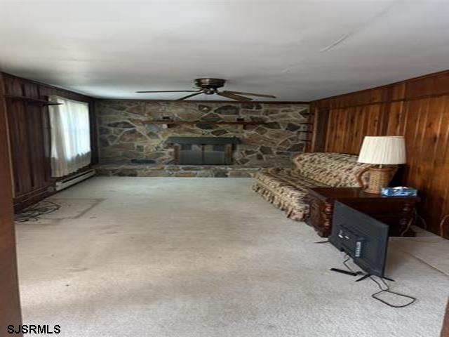 carpeted living room with a ceiling fan, wood walls, and a fireplace