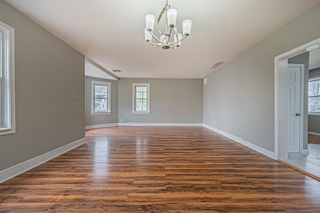 empty room with baseboards, visible vents, dark wood-style floors, and a notable chandelier