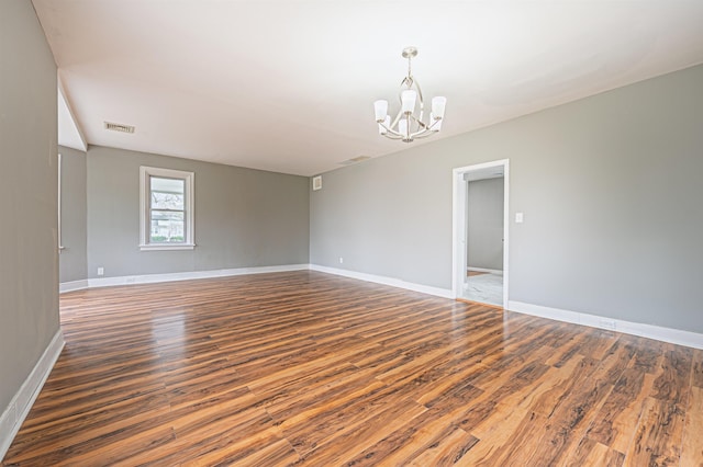 unfurnished room featuring baseboards, wood finished floors, visible vents, and a notable chandelier