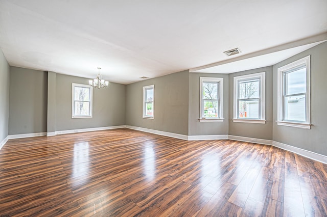 spare room with a notable chandelier, baseboards, a wealth of natural light, and dark wood-type flooring