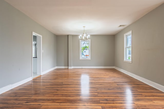 unfurnished room with wood finished floors, visible vents, baseboards, and an inviting chandelier