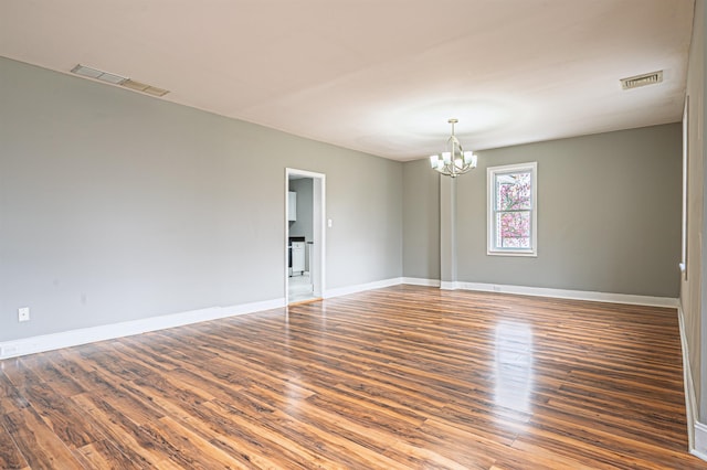 empty room with wood finished floors, visible vents, and an inviting chandelier