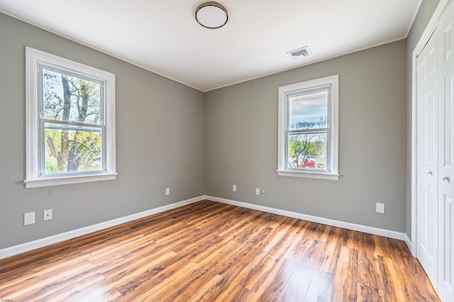 unfurnished bedroom with baseboards, wood finished floors, visible vents, and a closet