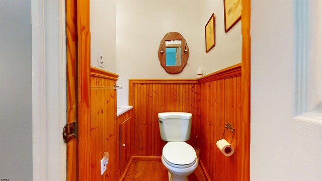 half bath with toilet, wood finished floors, and wooden walls