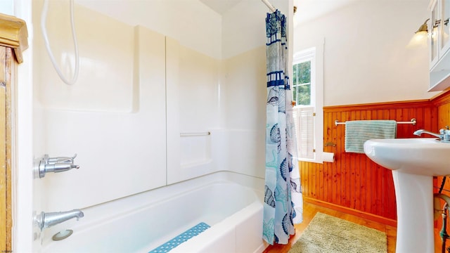 full bath with a wainscoted wall, wooden walls, wood finished floors, baseboards, and shower / bath combo