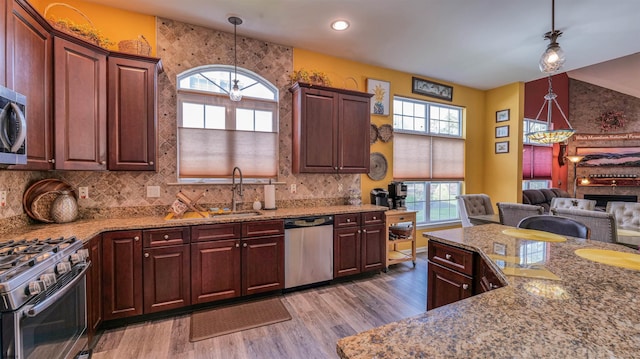 kitchen featuring tasteful backsplash, wood finished floors, stainless steel appliances, decorative light fixtures, and light stone countertops