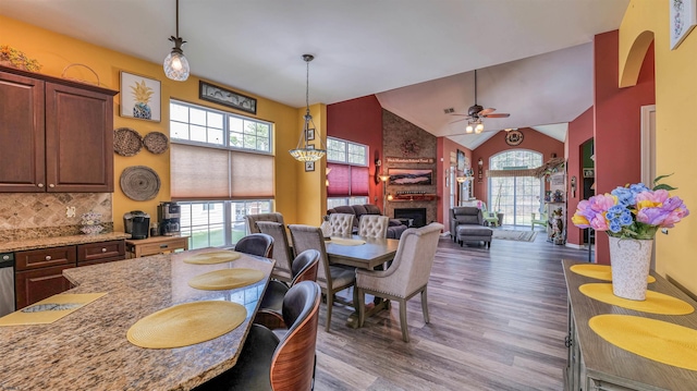 dining room with a fireplace, wood finished floors, high vaulted ceiling, and a healthy amount of sunlight