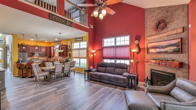 living room with recessed lighting, a towering ceiling, wood finished floors, a stone fireplace, and ceiling fan