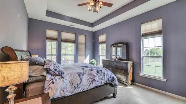 carpeted bedroom with visible vents, a ceiling fan, baseboards, and a raised ceiling