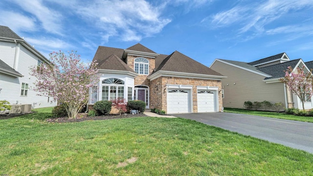 traditional-style house with central air condition unit, stone siding, an attached garage, a front yard, and aphalt driveway