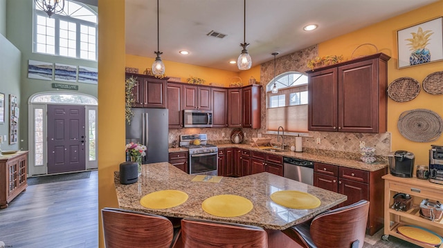 kitchen featuring a sink, pendant lighting, stainless steel appliances, a kitchen bar, and visible vents