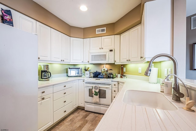 kitchen with white cabinetry, a sink, visible vents, light countertops, and white appliances