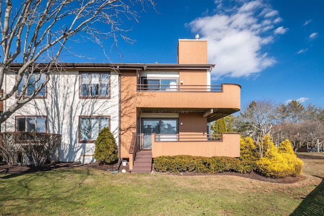 rear view of house featuring a chimney, a balcony, and a lawn