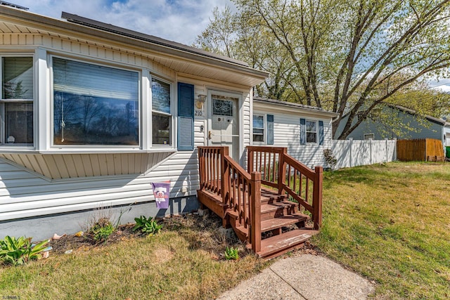 view of exterior entry featuring fence and a yard