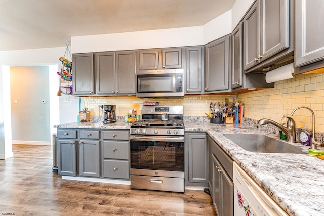 kitchen featuring wood finished floors, appliances with stainless steel finishes, backsplash, a sink, and gray cabinetry