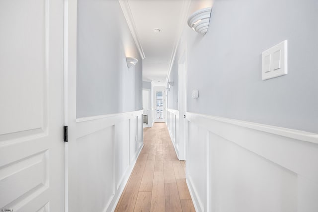 corridor featuring light wood-type flooring, crown molding, and wainscoting