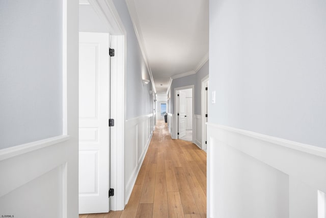 corridor with light wood-style floors, crown molding, and wainscoting