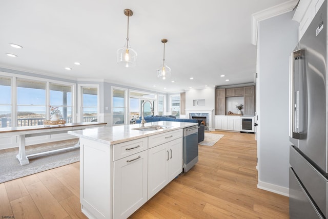 kitchen featuring light wood finished floors, a sink, a fireplace, ornamental molding, and appliances with stainless steel finishes