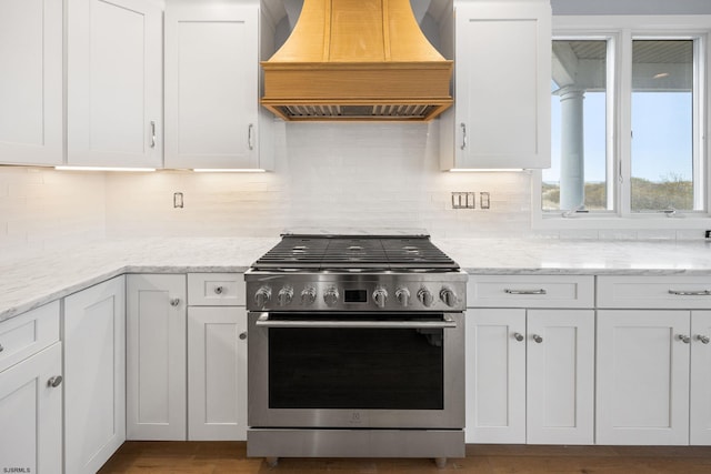 kitchen featuring high end range, custom range hood, and white cabinetry