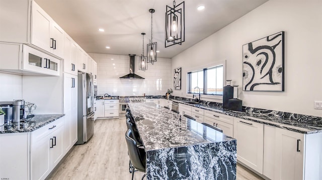 kitchen featuring dark stone counters, light wood-type flooring, a kitchen island, wall chimney range hood, and appliances with stainless steel finishes