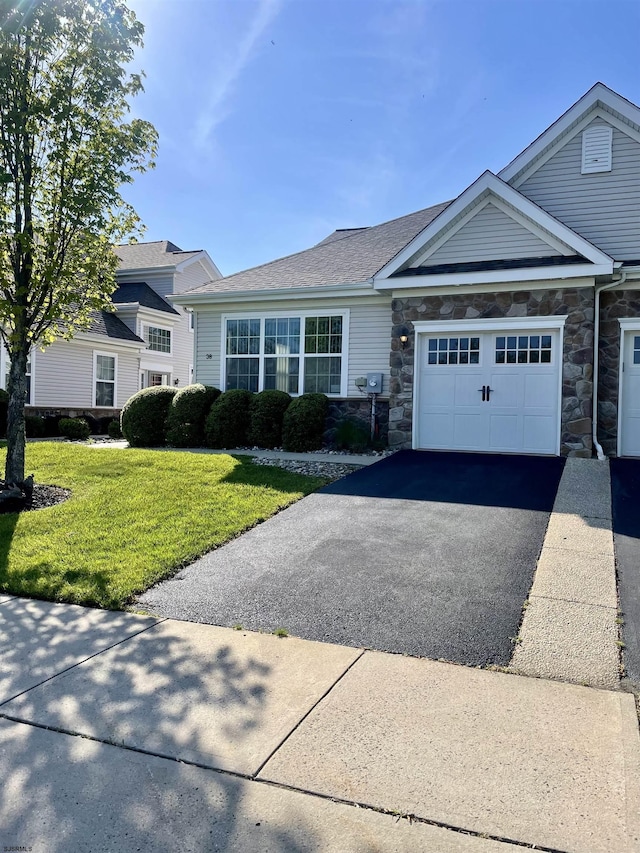 view of front of house featuring stone siding, aphalt driveway, a front lawn, and an attached garage