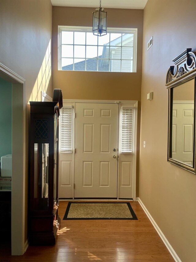 foyer with a chandelier, visible vents, baseboards, a towering ceiling, and wood finished floors