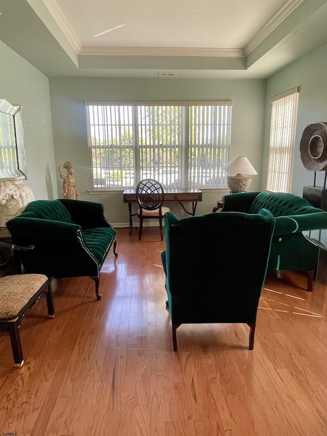 living area with ornamental molding, wood finished floors, and a tray ceiling