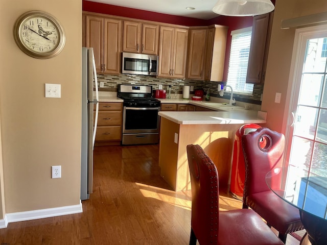 kitchen with appliances with stainless steel finishes, light countertops, a sink, a peninsula, and dark wood-type flooring