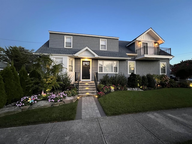view of front facade with a front yard, roof with shingles, and a balcony