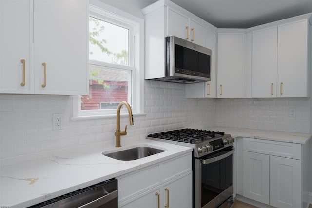kitchen featuring light stone counters, appliances with stainless steel finishes, white cabinets, backsplash, and a sink