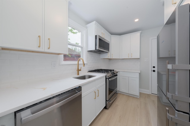 kitchen with light stone counters, white cabinets, a sink, stainless steel appliances, and light wood finished floors