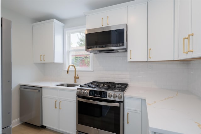 kitchen with light stone countertops, a sink, stainless steel appliances, backsplash, and white cabinets