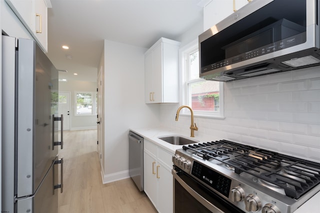 kitchen featuring a sink, stainless steel appliances, light wood-style floors, tasteful backsplash, and white cabinetry