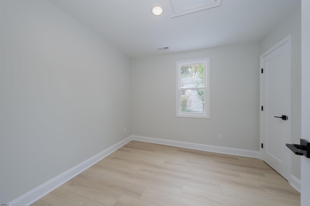 empty room with attic access, visible vents, light wood-type flooring, and baseboards