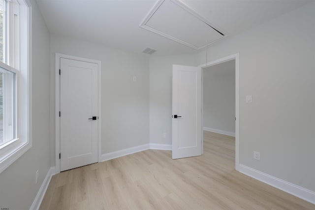 unfurnished bedroom with baseboards, light wood-type flooring, and attic access