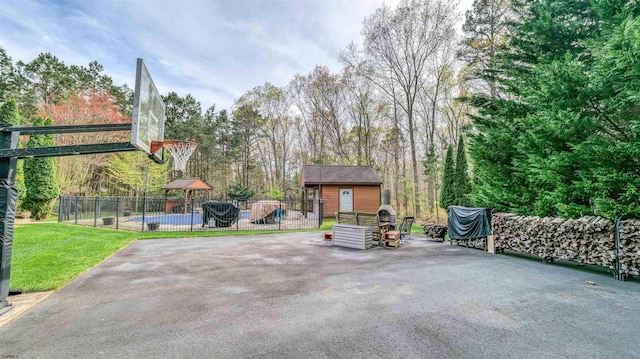 view of patio with an outdoor structure, a playground, a swimming pool, basketball court, and fence