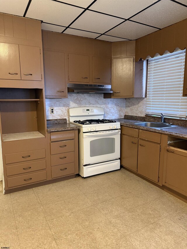 kitchen with a paneled ceiling, a sink, under cabinet range hood, white gas stove, and dark countertops