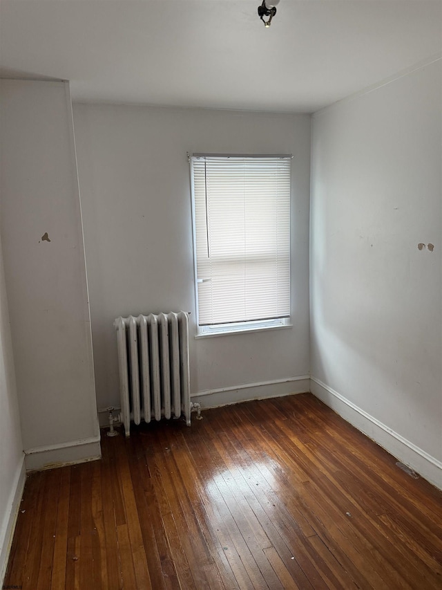 spare room featuring radiator heating unit, hardwood / wood-style flooring, and baseboards