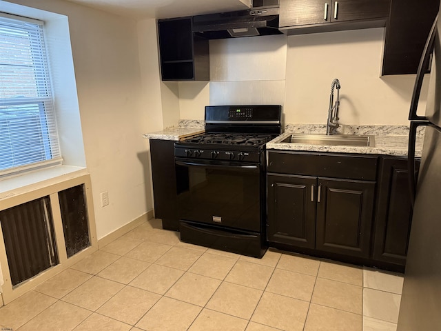 kitchen featuring a sink, under cabinet range hood, light tile patterned floors, black gas stove, and freestanding refrigerator