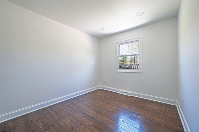 unfurnished room with baseboards, dark wood-style floors, and visible vents