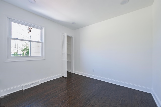 unfurnished room with baseboards, dark wood-style flooring, and visible vents