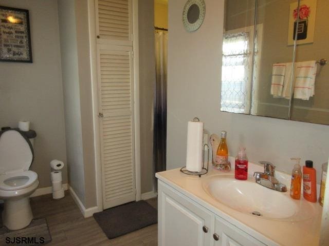 full bathroom featuring a closet, vanity, wood finished floors, toilet, and baseboards