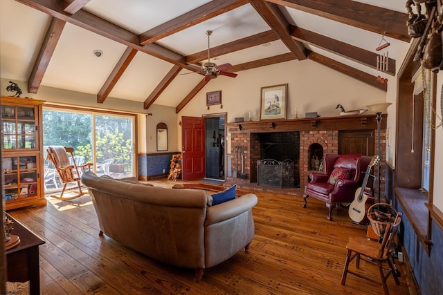 living area with vaulted ceiling with beams, wood-type flooring, a brick fireplace, and ceiling fan