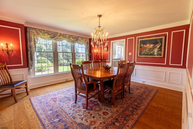 dining space with crown molding, wainscoting, a decorative wall, a chandelier, and light wood-type flooring