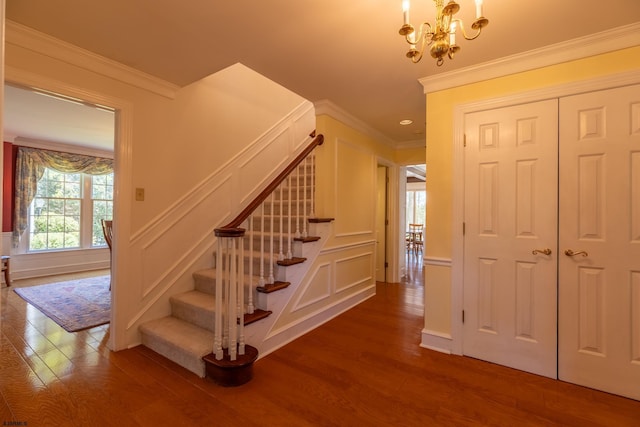 stairs featuring wood finished floors, ornamental molding, a decorative wall, and a chandelier