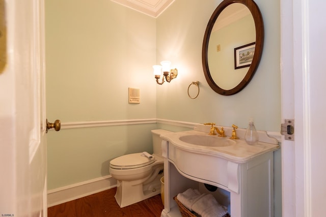 half bath with crown molding, vanity, toilet, baseboards, and wood finished floors