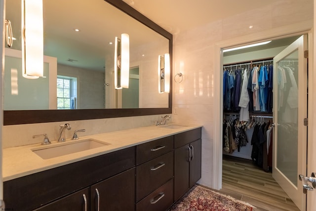 bathroom featuring double vanity, a sink, a walk in closet, and wood finished floors